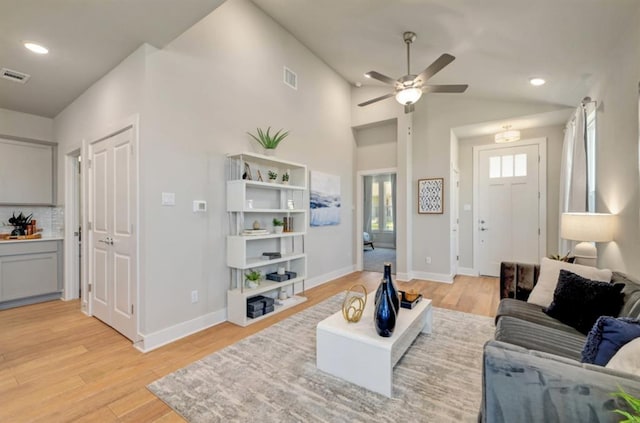 living room with light wood-style floors, visible vents, vaulted ceiling, and baseboards