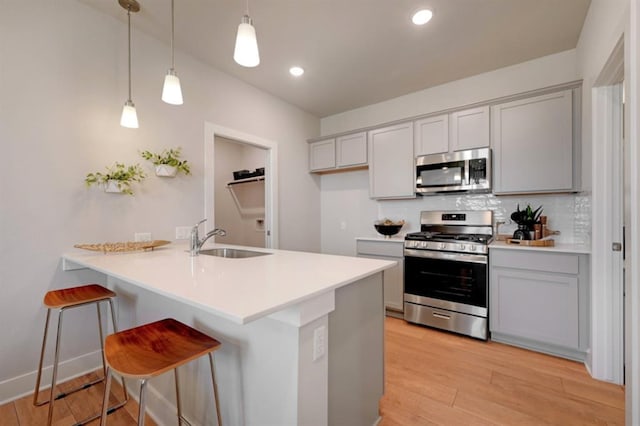 kitchen with stainless steel appliances, tasteful backsplash, light wood-style floors, a sink, and a peninsula