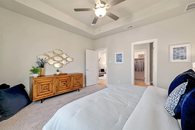 bedroom with light carpet, a raised ceiling, visible vents, and a ceiling fan