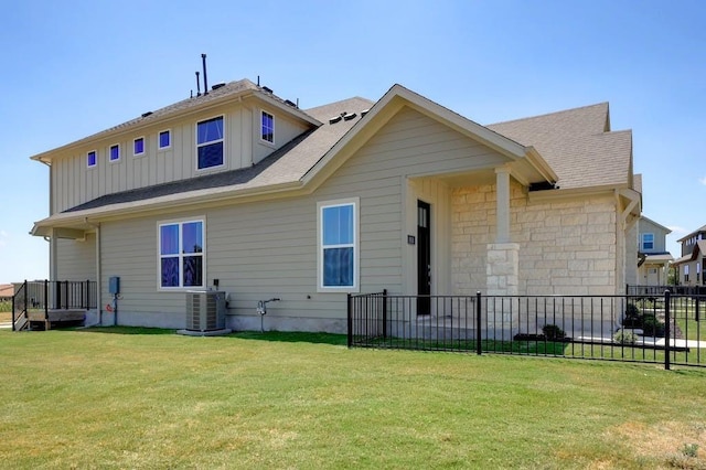 back of house featuring a lawn, board and batten siding, central AC, fence, and stone siding