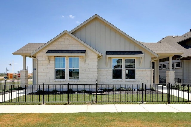 view of front of house with a fenced front yard, stone siding, a shingled roof, and board and batten siding