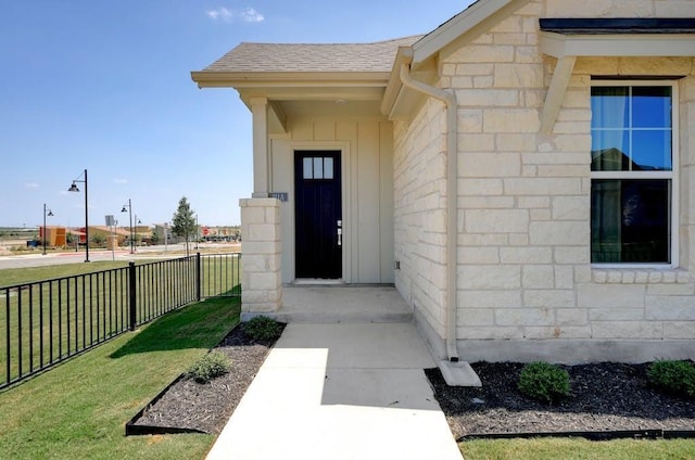 doorway to property with stone siding, a yard, roof with shingles, and fence