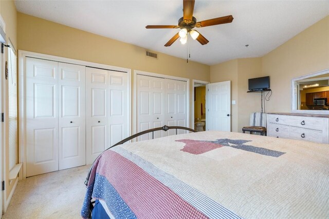 bedroom with visible vents, a ceiling fan, multiple closets, and light carpet