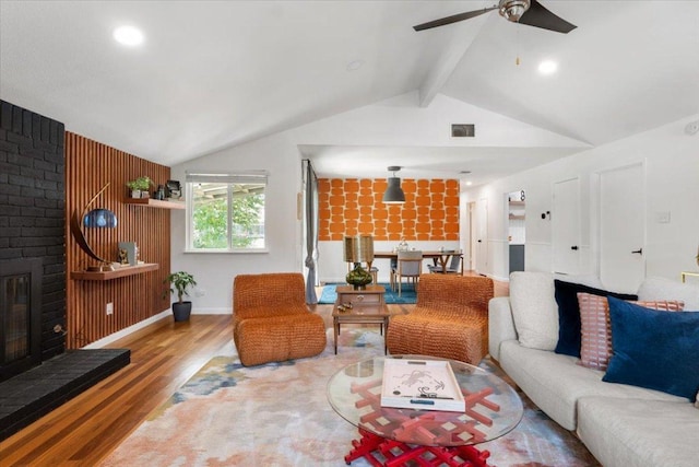 living area featuring vaulted ceiling with beams, a brick fireplace, visible vents, and wood finished floors