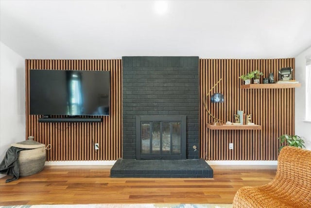 living room with a brick fireplace, baseboards, wood finished floors, and wood walls