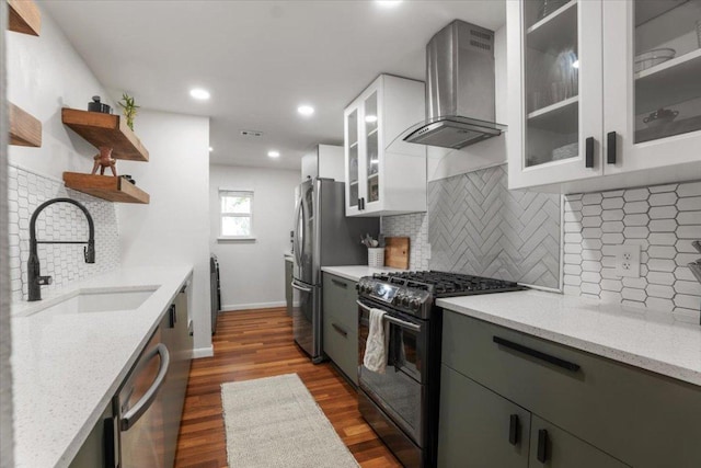 kitchen with light stone counters, open shelves, stainless steel appliances, a sink, and wall chimney range hood