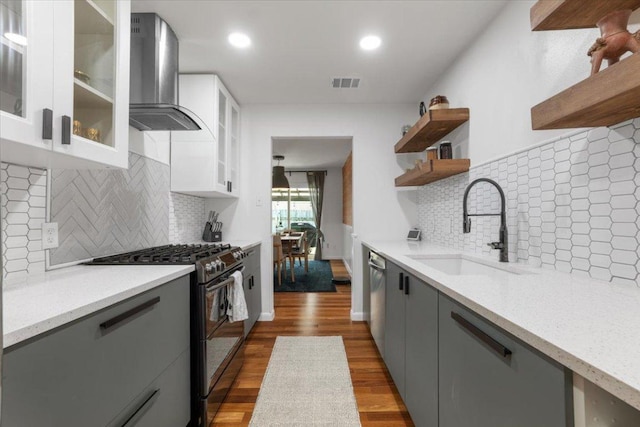 kitchen with open shelves, stainless steel appliances, visible vents, a sink, and wall chimney range hood