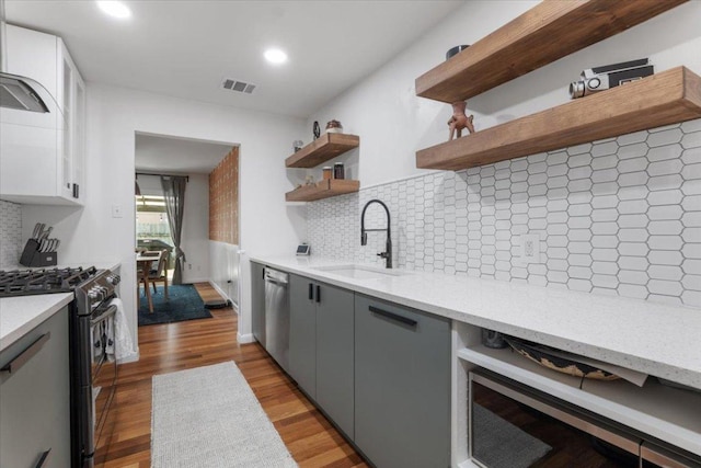 kitchen featuring gray cabinetry, a sink, light wood-style floors, open shelves, and black gas range oven