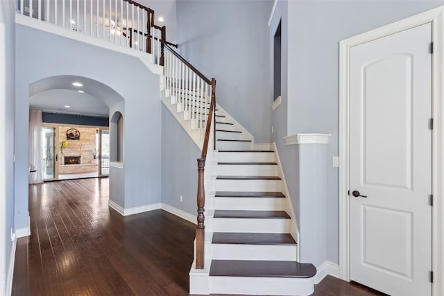 606 Anfield Cir, Austin, TX 78738 - stairway featuring wood-type flooring, arched walkways, a high ceiling, and a stone fireplace