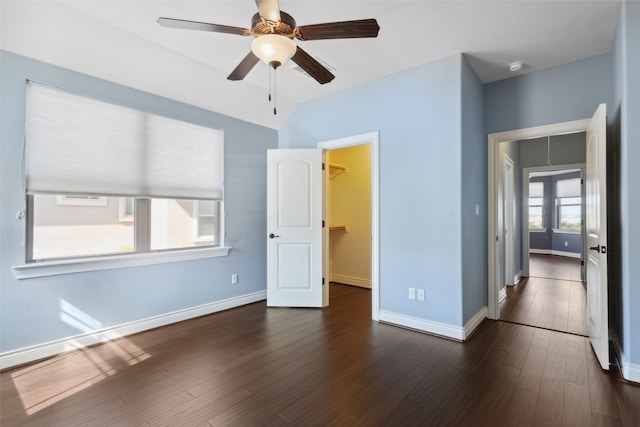 unfurnished bedroom featuring a walk in closet, baseboards, dark wood-style flooring, and ceiling fan