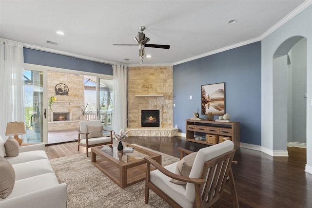 living area featuring wood finished floors, visible vents, arched walkways, ornamental molding, and a stone fireplace