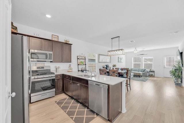 kitchen with light wood finished floors, a peninsula, stainless steel appliances, dark brown cabinets, and a sink