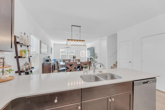 kitchen with a sink, open floor plan, light countertops, stainless steel dishwasher, and hanging light fixtures