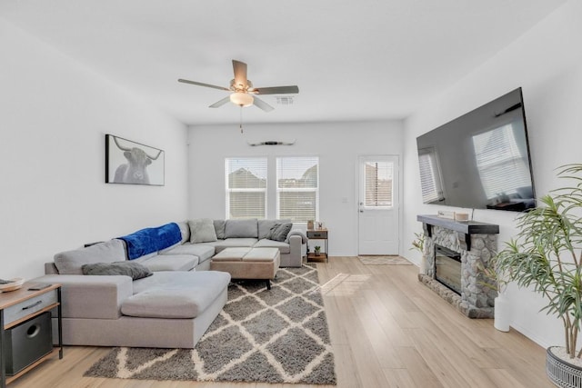 living room featuring ceiling fan, light wood finished floors, a fireplace, and visible vents