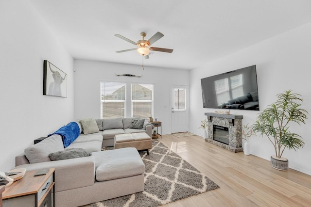 living room featuring baseboards, a ceiling fan, wood finished floors, and a stone fireplace