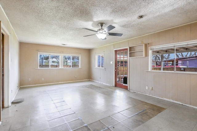 spare room with a ceiling fan, wood walls, and a textured ceiling