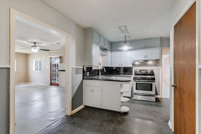 kitchen with stainless steel range with gas cooktop, dark countertops, a sink, a textured ceiling, and under cabinet range hood