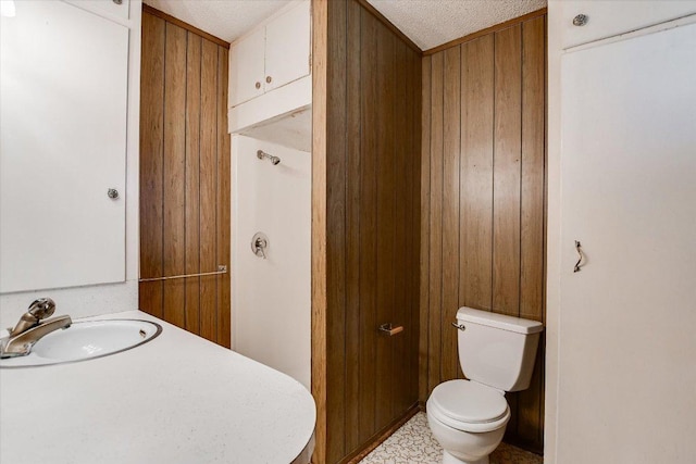 bathroom featuring a textured ceiling, a sink, toilet, and wooden walls