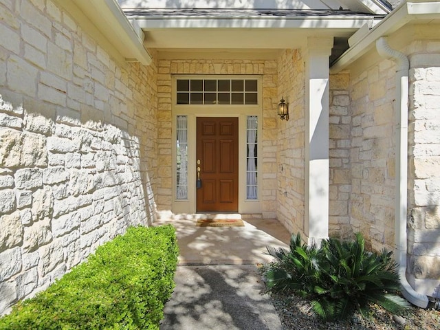 entrance to property with stone siding and roof with shingles