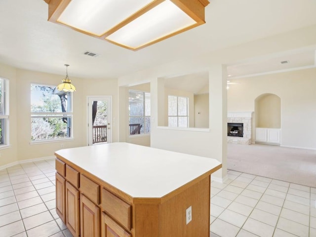 kitchen with light countertops, hanging light fixtures, light tile patterned flooring, a kitchen island, and a stone fireplace