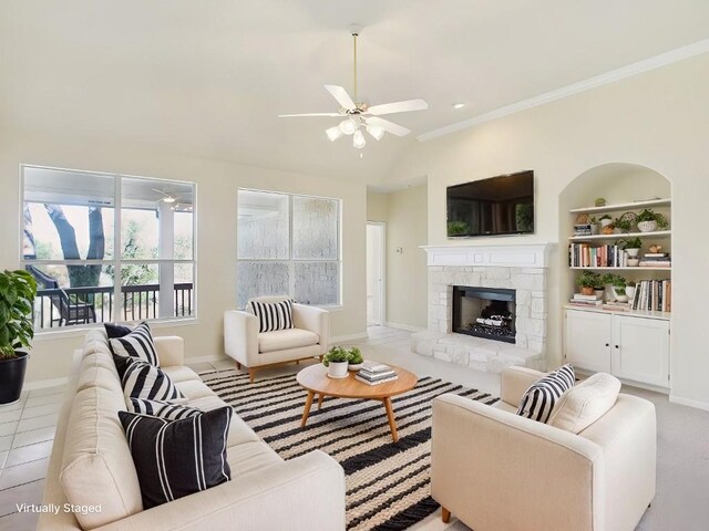 living room with built in shelves, a fireplace, a ceiling fan, baseboards, and crown molding