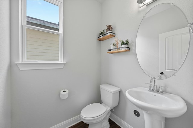 half bathroom featuring toilet, baseboards, a sink, and wood finished floors