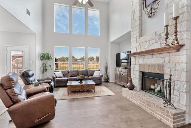 living room featuring a fireplace with raised hearth, plenty of natural light, wood finished floors, and visible vents