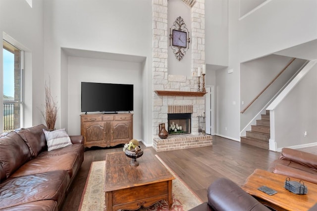 living room featuring stairs, a high ceiling, wood finished floors, and a stone fireplace