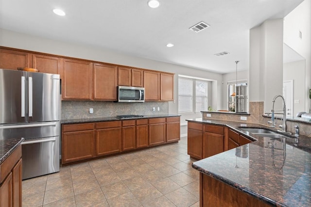 kitchen featuring stainless steel appliances, tasteful backsplash, visible vents, brown cabinetry, and a sink