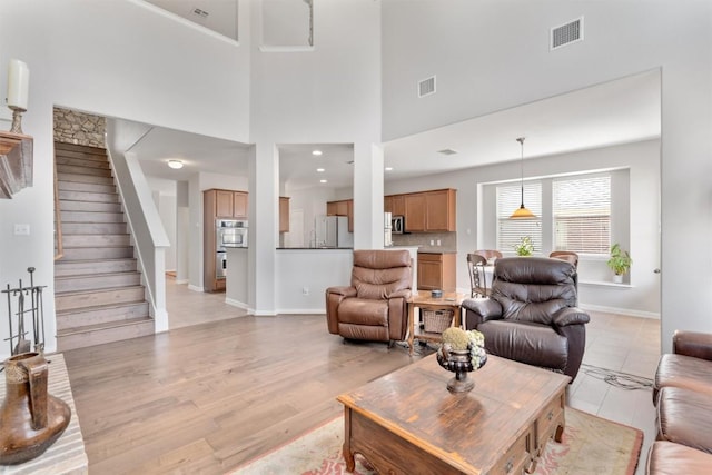 living area with stairway, baseboards, visible vents, and light wood finished floors