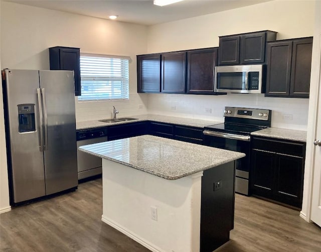 kitchen with wood finished floors, a sink, a center island, appliances with stainless steel finishes, and decorative backsplash