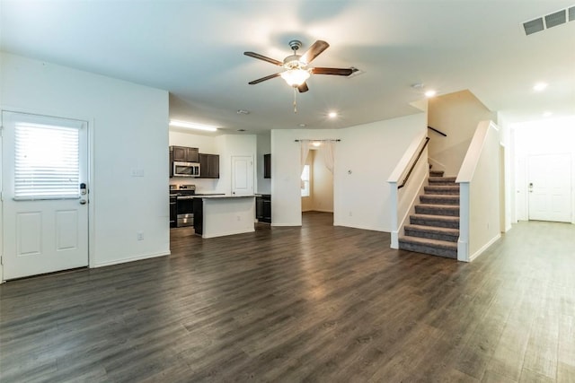 unfurnished living room featuring dark wood-type flooring, visible vents, ceiling fan, and stairs