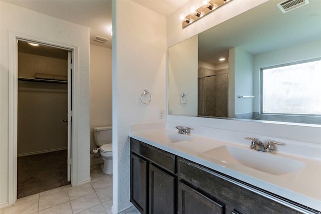 bathroom featuring tile patterned flooring, toilet, a sink, visible vents, and tiled shower