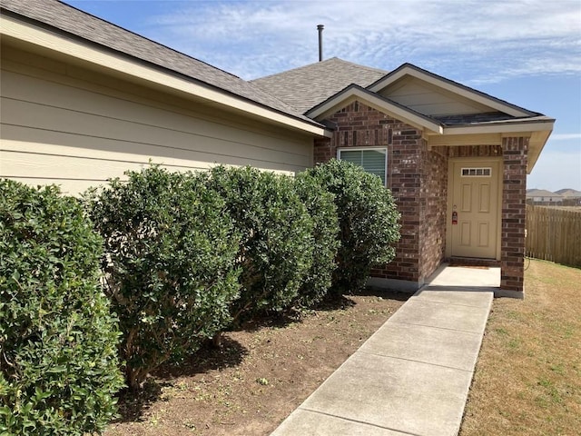 property entrance with a shingled roof, fence, and brick siding