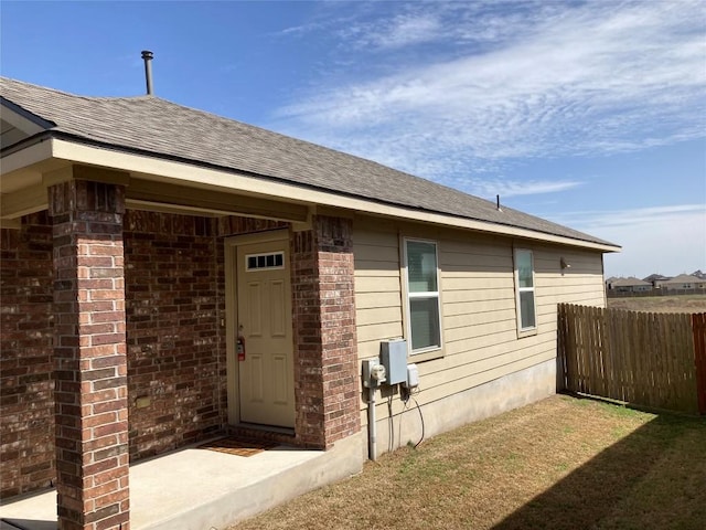 exterior space featuring brick siding, fence, and roof with shingles