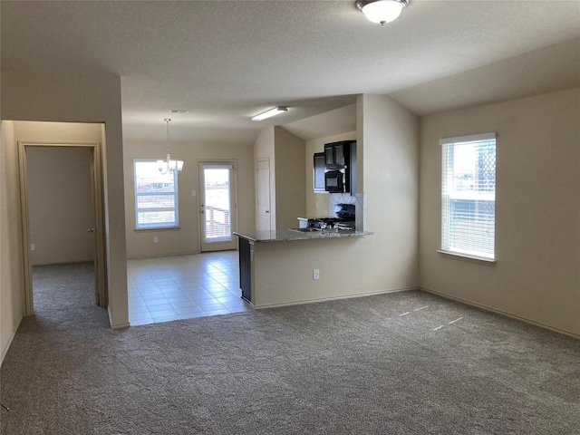 unfurnished living room featuring plenty of natural light, a chandelier, vaulted ceiling, and light colored carpet