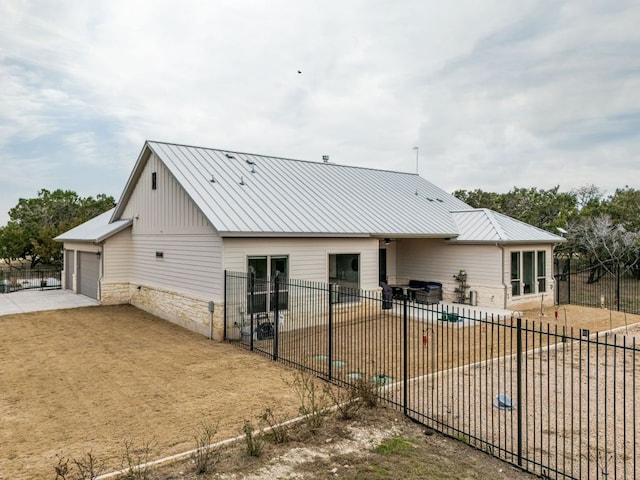 exterior space with metal roof, fence private yard, stone siding, concrete driveway, and a patio area