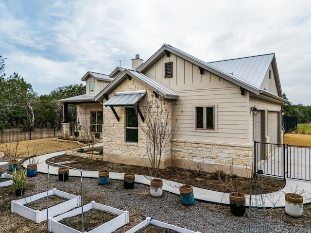 back of house featuring stone siding, a vegetable garden, metal roof, and board and batten siding