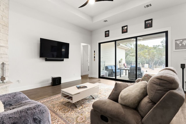 living area featuring a raised ceiling, wood finished floors, visible vents, and baseboards