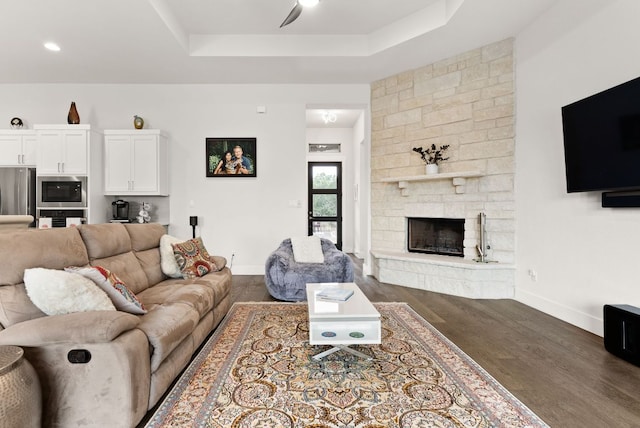 living area with baseboards, a ceiling fan, wood finished floors, a tray ceiling, and a fireplace