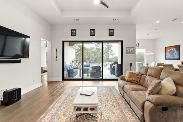 living room featuring light wood-style floors, a tray ceiling, visible vents, and baseboards