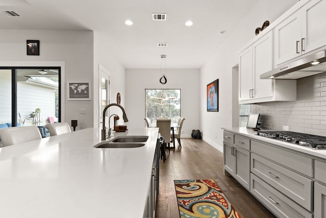 kitchen with visible vents, a sink, under cabinet range hood, stainless steel gas stovetop, and backsplash