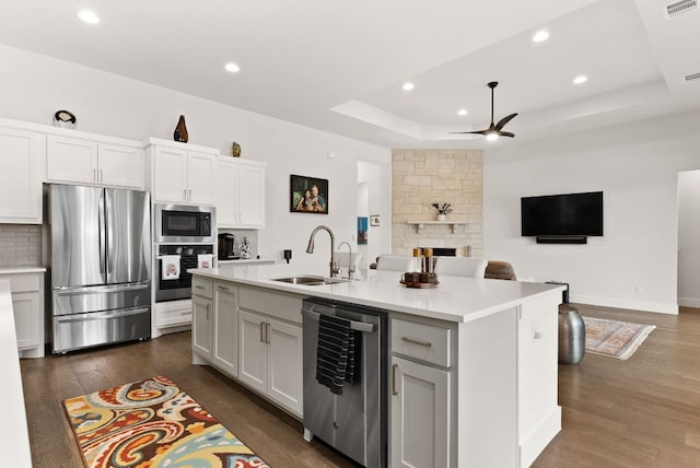 kitchen featuring dark wood finished floors, a raised ceiling, appliances with stainless steel finishes, open floor plan, and a sink