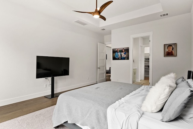 bedroom with baseboards, visible vents, a raised ceiling, and wood finished floors