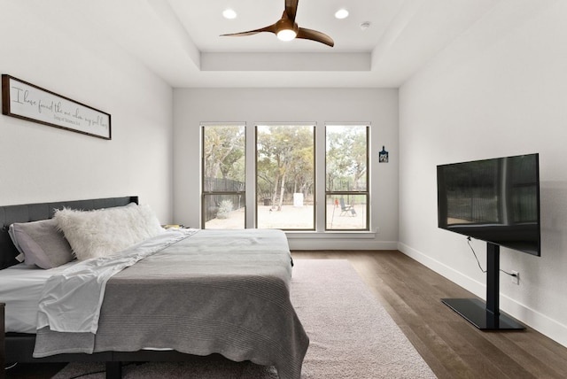 bedroom with a tray ceiling, recessed lighting, a ceiling fan, wood finished floors, and baseboards