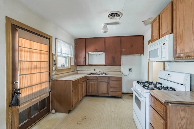 kitchen with white appliances, visible vents, brown cabinetry, light countertops, and a sink