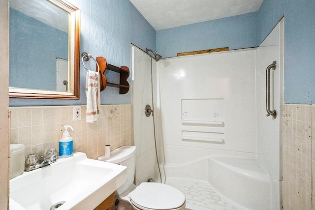 bathroom featuring a wainscoted wall, tile walls, toilet, a stall shower, and a sink