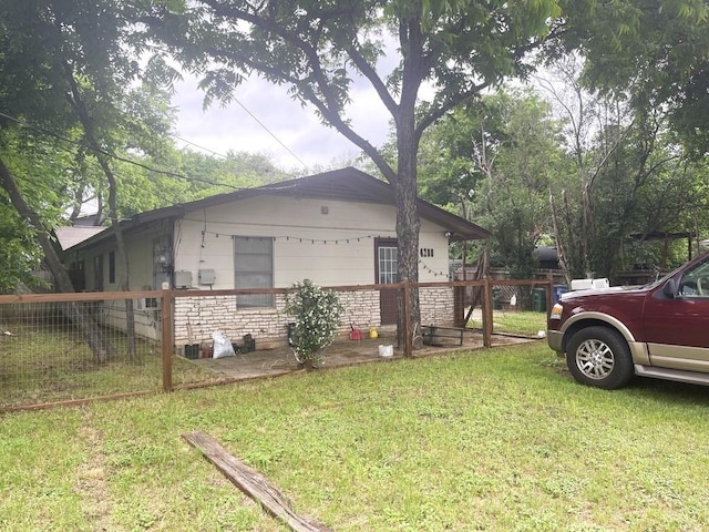 view of side of property with stone siding, a yard, and fence