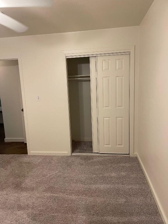 unfurnished bedroom featuring baseboards, dark carpet, and a closet