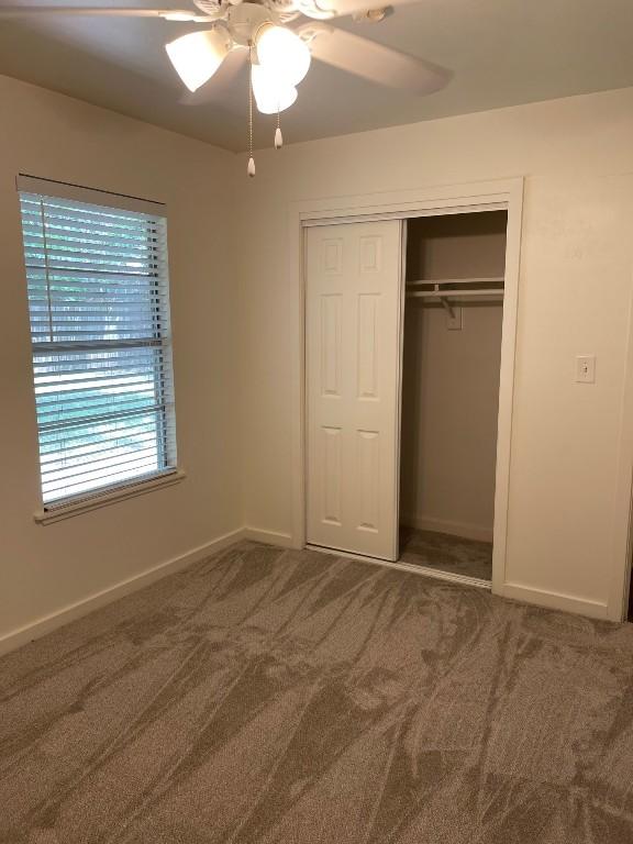 unfurnished bedroom with ceiling fan, a closet, baseboards, and carpet flooring